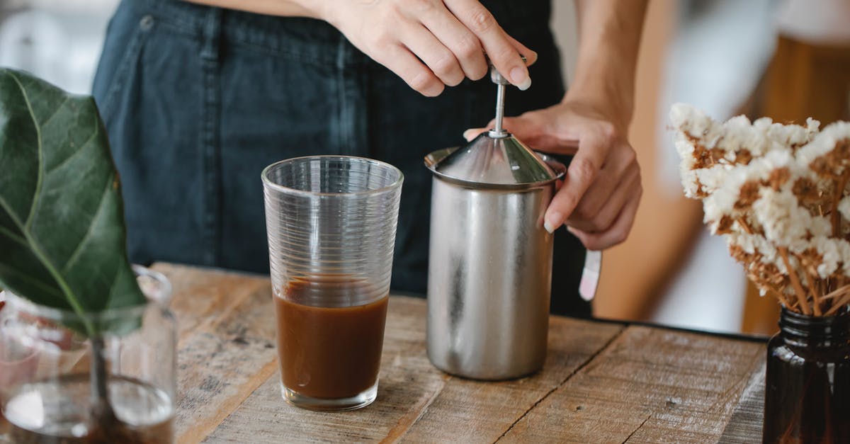 Is there any botulism risk in homemade cold brew coffee? - Crop anonymous female barista making froth in manual steel milk frother while preparing iced chocolate coffee in light kitchen