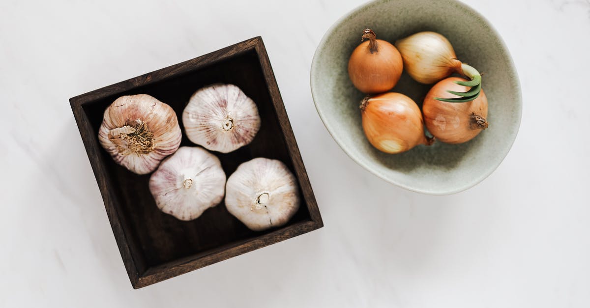 Is there any food ingredient that tastes like diesel smells? - Overhead of square pot with fresh unpeeled garlic near light green bowl with raw yellow onions against white marble surface