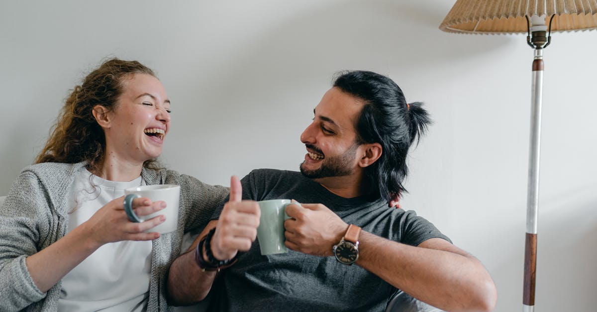 Is there some drink like panaché available in the Netherlands? - Positive girlfriend in casual wear looking at content ethnic man in smart watch while sitting on cozy sofa with cups of hot beverage and looking at each other