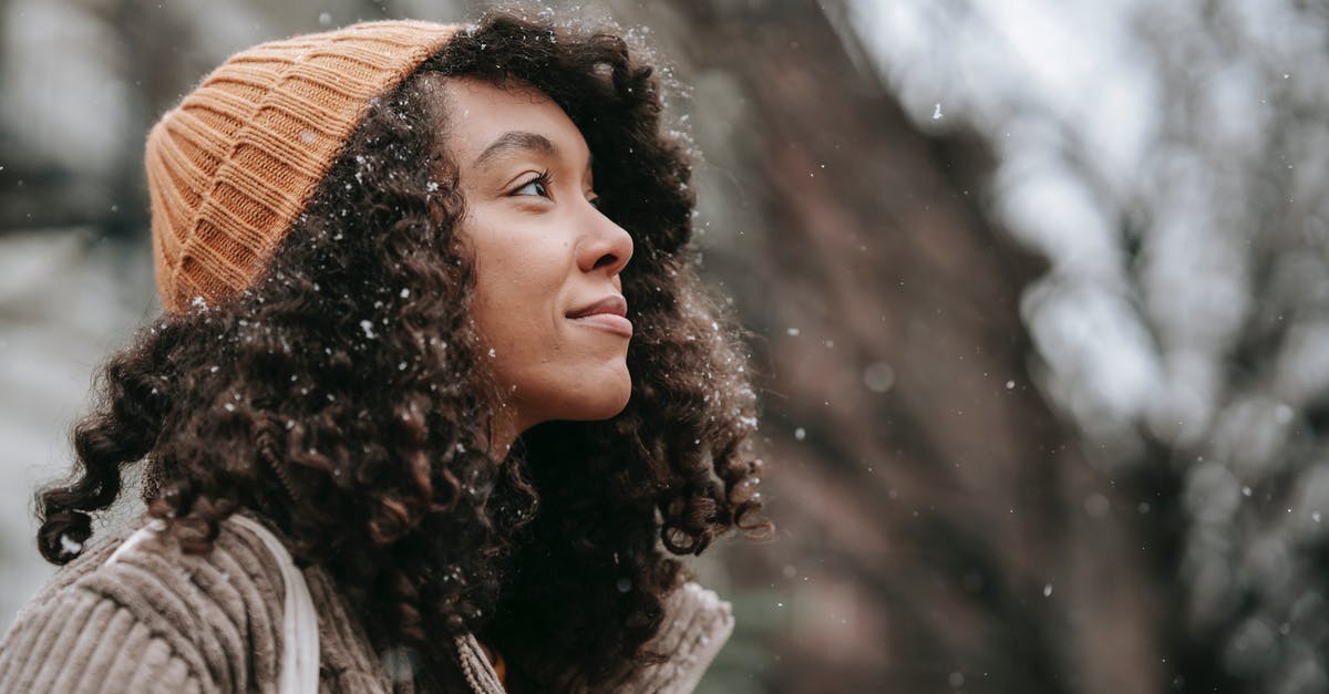 Is this some kind of warming oven? - Side view of dreamy young black female in knitted hat looking up in town on snowy day