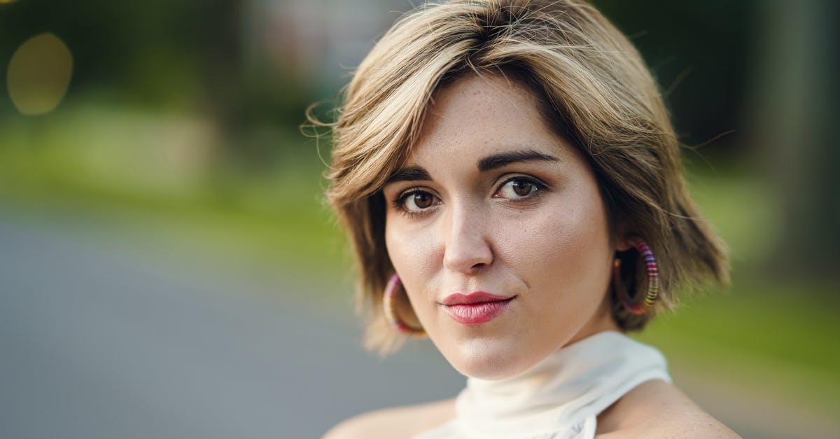 Is this the way to make good pies? - Headshot of attractive female wearing white outfit and earrings standing near asphalt road and grassy lawn on blurred background in city with bokeh