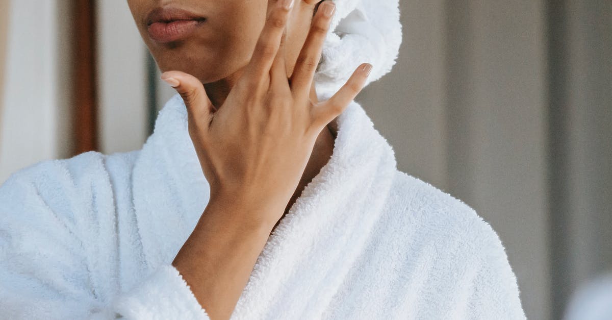 Is unsour sour cream too new or too old? - Crop anonymous female in white bathrobe with towel on head applying facial moisturizing cream on face while standing in bathroom