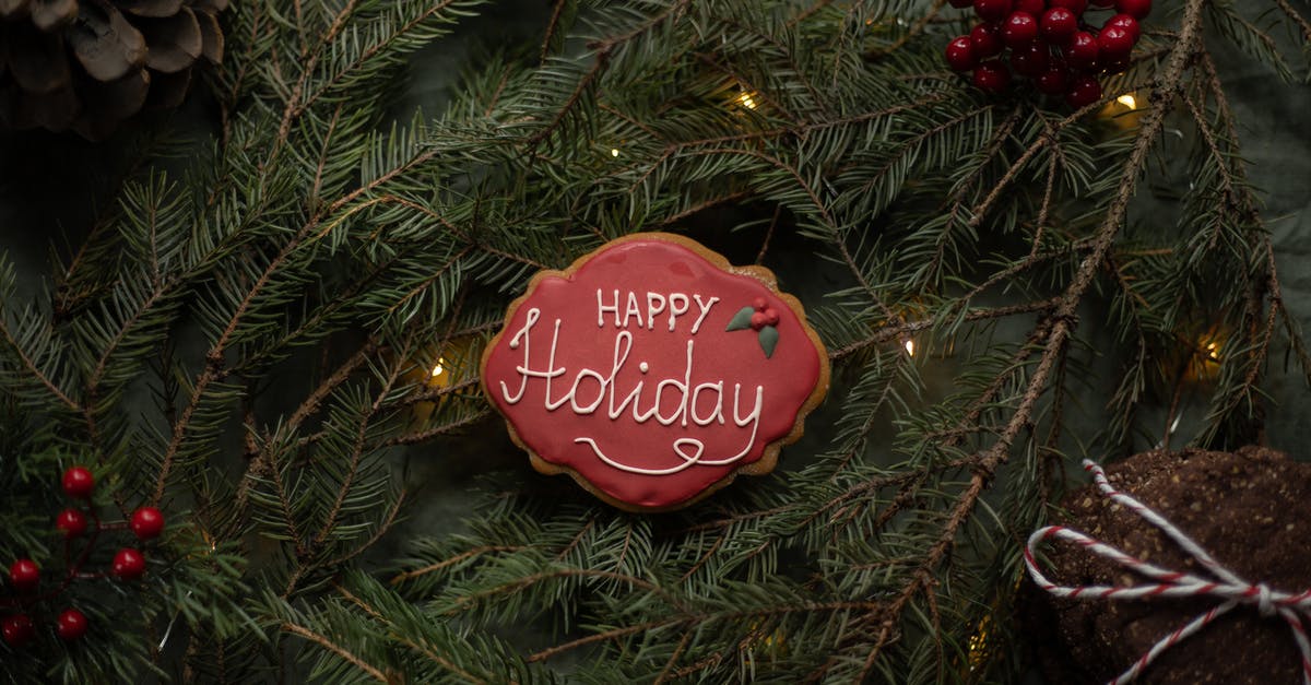 Is using chocolate instead of royal icing for a gingerbread house more difficult? - Happy Holiday inscription on biscuit on fir sprigs with garland