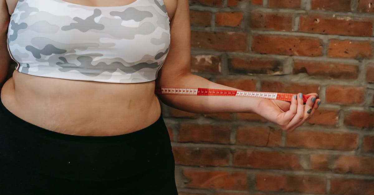 Isn't moisture a problem when measuring flour by weight? - Crop anonymous plump female using measuring tape for measuring belly near brick wall