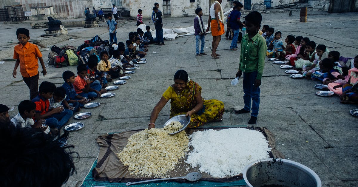 Keeping bugs out of rice - From above of old Indian woman serving food on plates while sitting on ground surrounded with kids in poor area