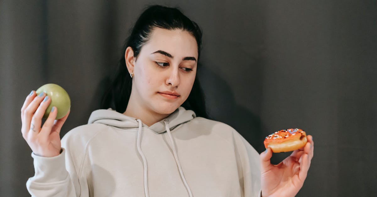 Keeping Donuts fresh - Thoughtful woman choosing between green apple and sweet donut