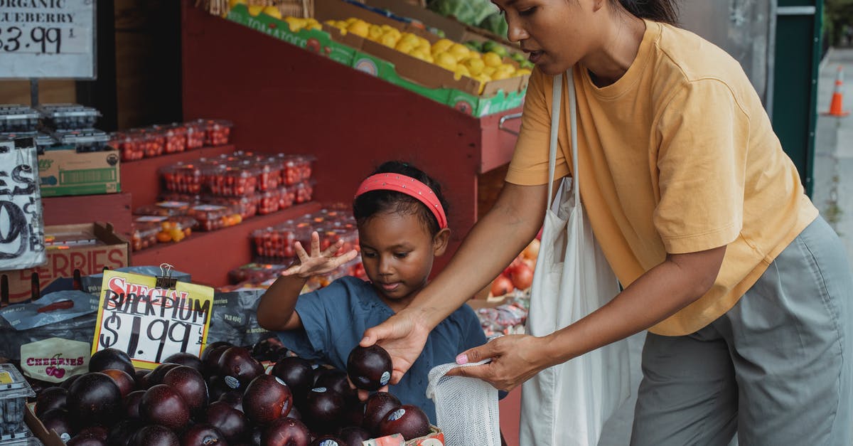 Kids Lunch box - suggestion for fruit smoothie packaging - Asian woman putting black plum into eco bag while choosing fruits from box in street market with daughter