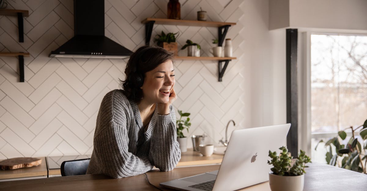 Kitchen clambake using kombu? - Young cheerful female smiling and talking via laptop while sitting at wooden table in cozy kitchen