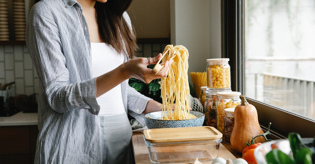 Kitchen utensil identification - tong of some sort - Side view of cheerful female with long cooked spaghetti on tongs standing in kitchen while preparing delicious pasta at home