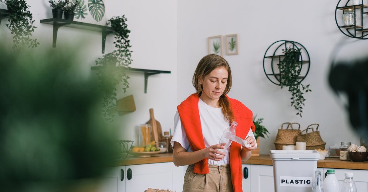 Kitchen utensil identification - tong of some sort - Calm woman in casual clothes standing near table and cleaning plastic bottle while sorting rubbish in light kitchen in daytime