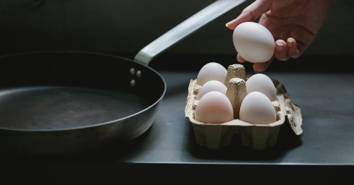 Lasagne package says cook from frozen - High angle of crop anonymous housewife with uncooked chicken egg from container placed near pan