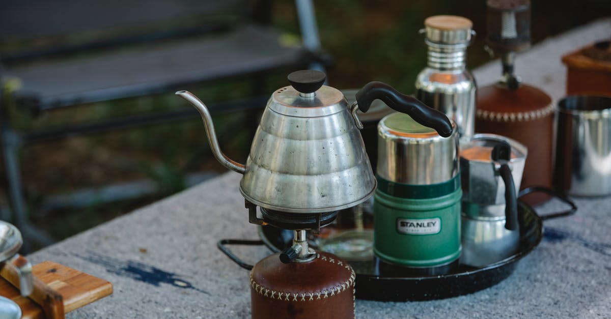 Leaving empty cast iron pot on a gas stove - High angle of metal coffee kettle placed on small portable camping gas stove near various utensils on table in nature