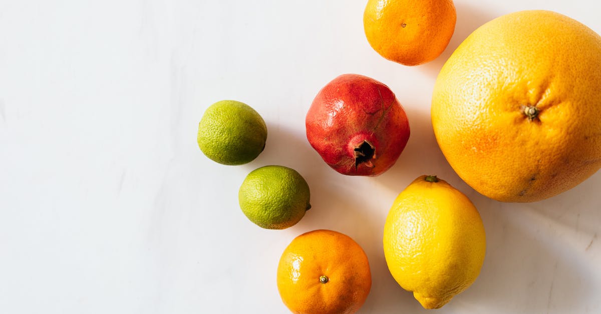 Lemon turned broccoli purple - Top view closeup of whole ripe limes and tangerines and lemon and pomegranate and grapefruit arranged randomly on white surface