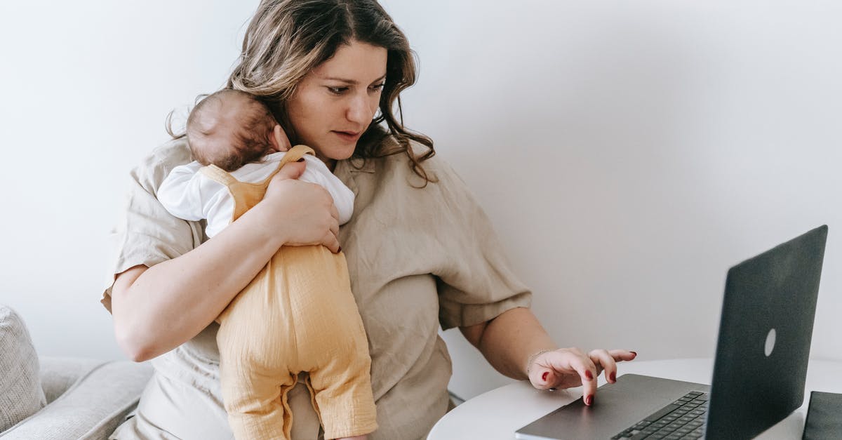 Lentils and barley used together - Concentrated young female freelancer embracing newborn while sitting at table and working remotely on laptop at home