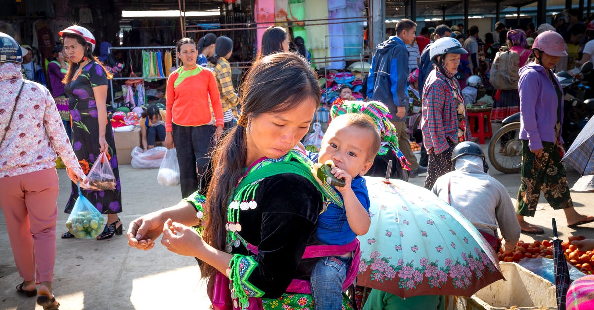 Less sticky rice and lentils - Young Asian mom with toddler child eating tasty sweet rice in banana leaf against anonymous shoppers in urban bazaar