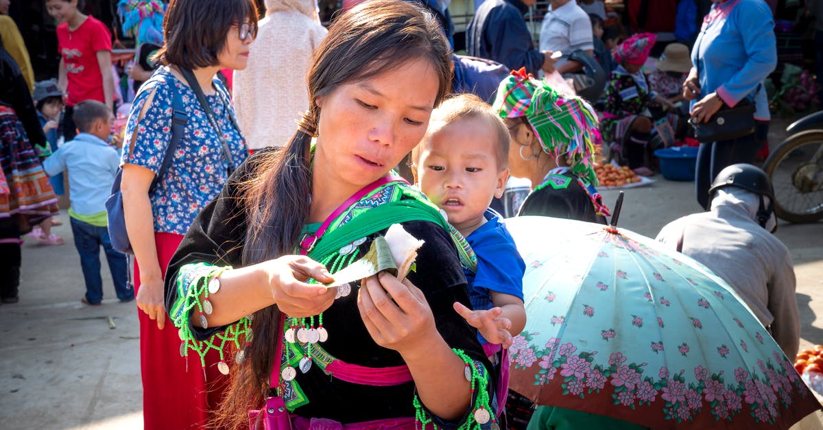 Less sticky rice and lentils - Young ethnic mom in traditional wear with baby and sticky rice in banana leaf in urban market