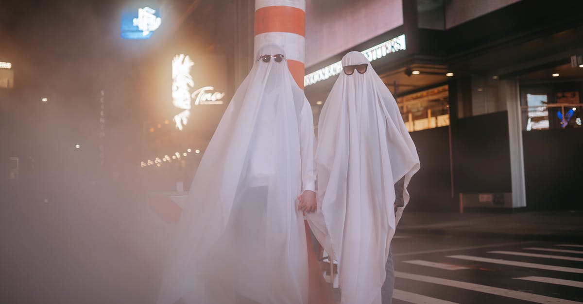 Lobster, steamed Saturday afternoon, eaten Monday night? - Anonymous couple wearing ghost costumes and sunglasses holding hands while standing near steam pipe and building in night city during Halloween