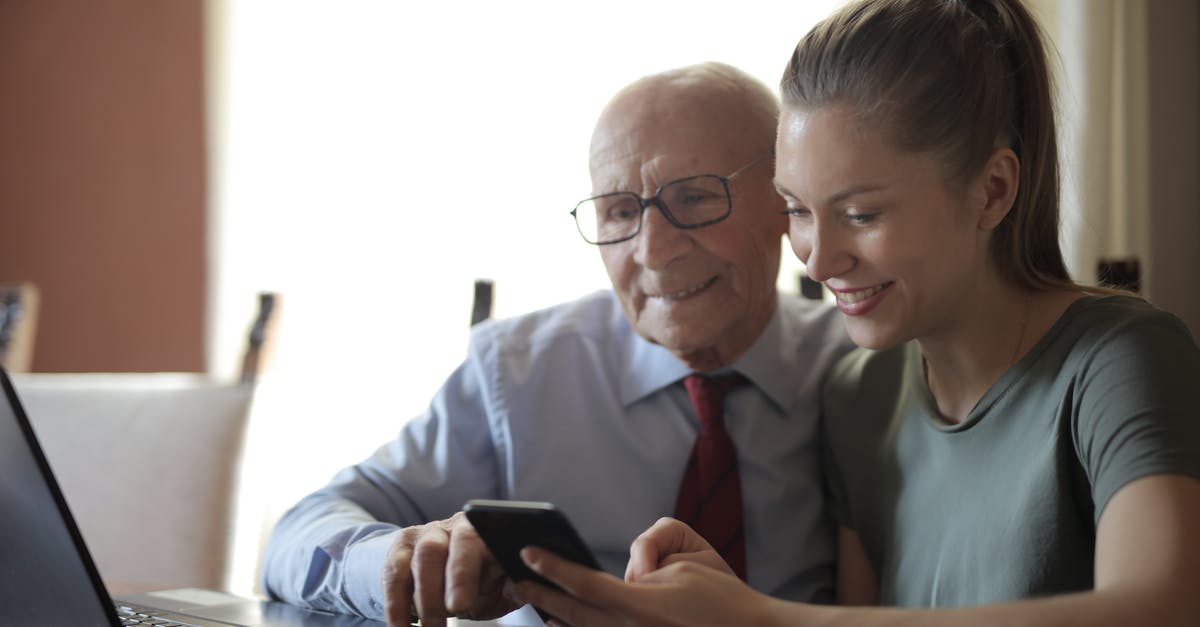 Looking for a recipe generator [duplicate] - Positive senior man in formal shirt and eyeglasses and smiling young granddaughter sharing mobile phone while sitting near laptop at table