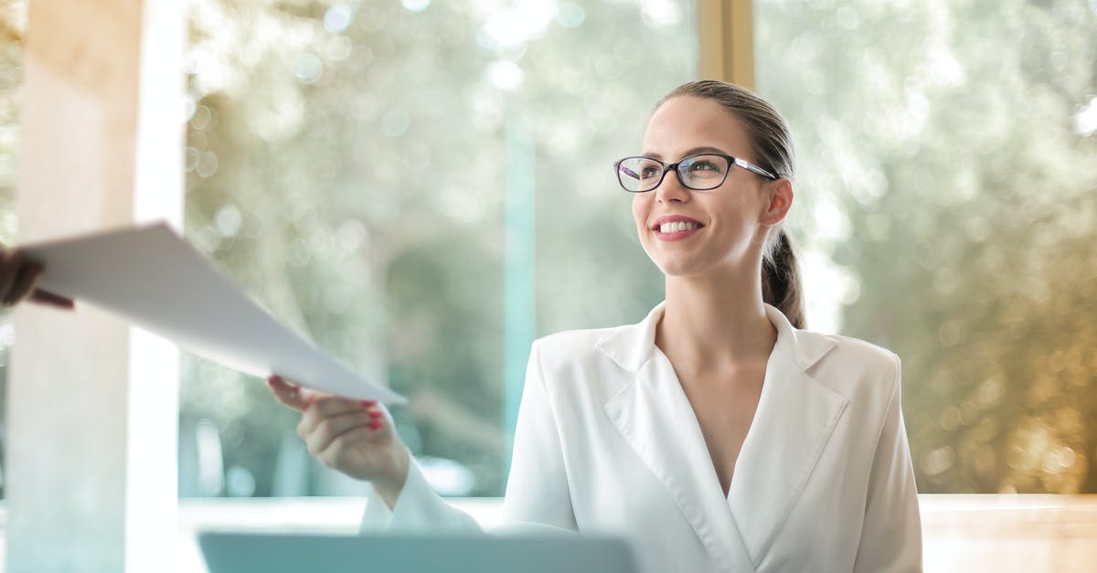 looking for edible paper - Low angle of successful female executive manager in classy style sitting at table with laptop in contemporary workplace and passing documents to colleague