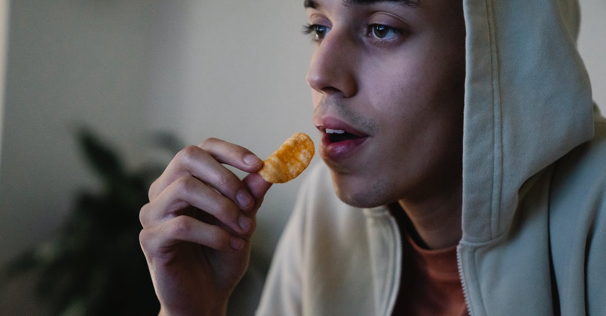 Looking for the name of an orange crunchy snack - Crop focused young ethnic male in hoodie with crispy potato chip looking forward in house room