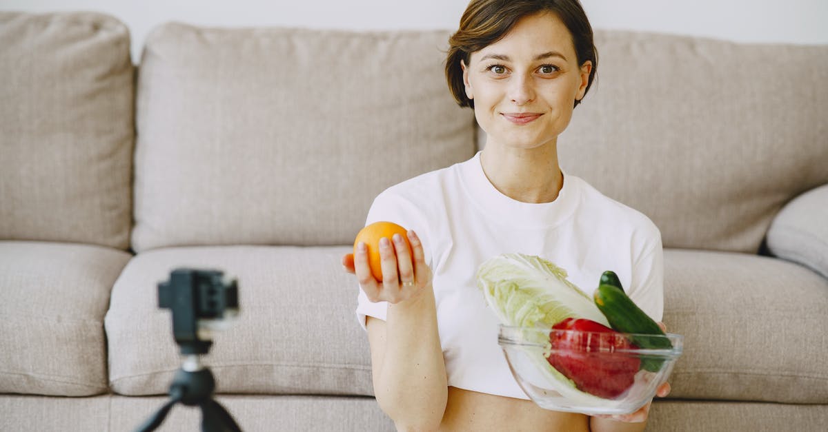 Looking for the name of an orange crunchy snack - Optimistic female in white clothes sitting near sofa and holding bowl with fresh vegetables and orange in hands and looking at camera