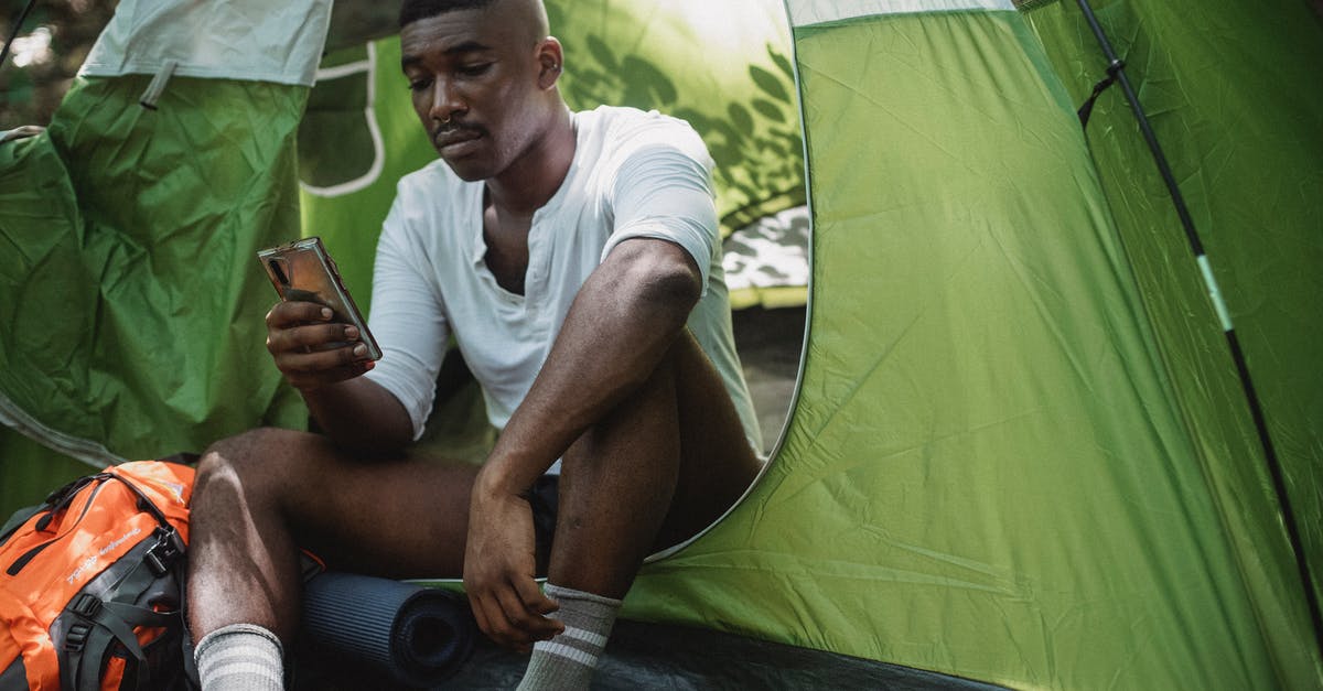 Looks curdled, but it wasn't - my bad alfredo - Sad African American male traveler resting in tent and browsing Internet on cellphone while spending journey in nature