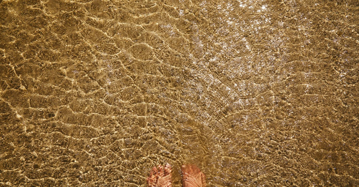 Lots of liquid in bottom of wok when stir frying - Top view of crop anonymous barefoot female standing in pure transparent rippling water of sea with sandy bottom