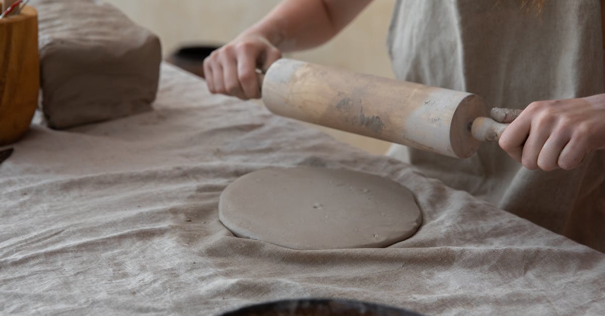 Make spring rolls in advance - Crop anonymous female artisan in apron rolling out clay slab on table while creating in light pottery