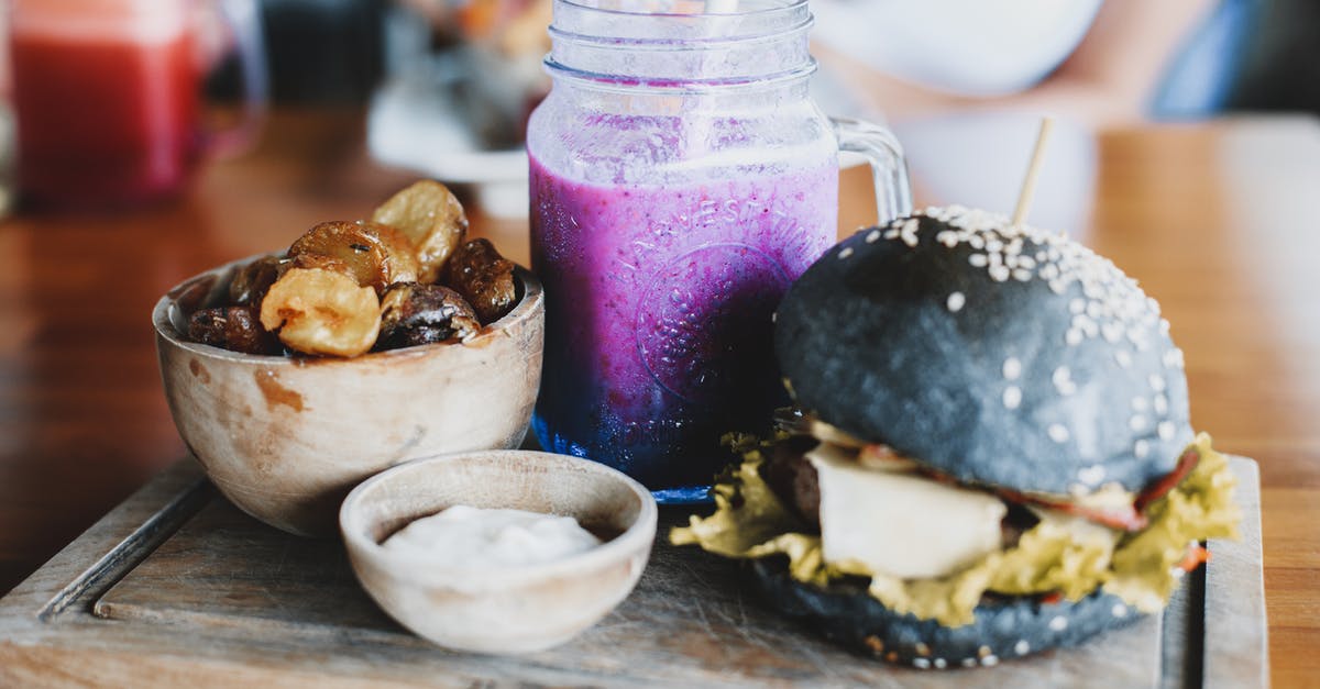 making a detox smoothie more palatable - Delicious black burger with freshly made purple smoothie and wooden bowl of dried bananas and dates served on wooden board in cafe