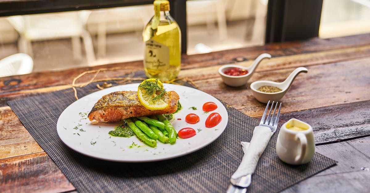 Making lemon oil from vodka - High angle of served plate with fried fish and vegetables placed near saucers with spices and olive oil