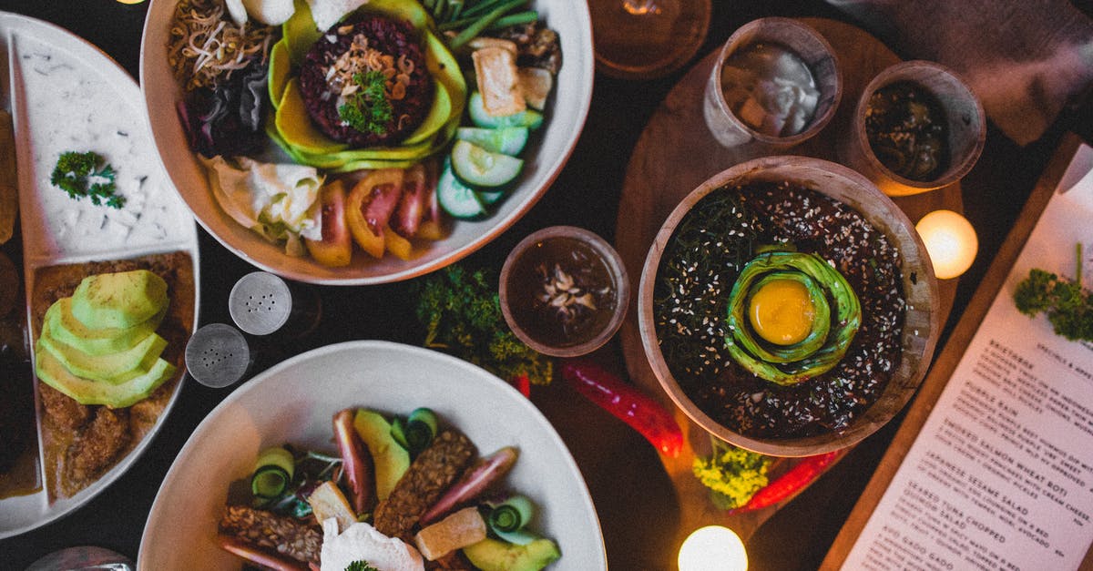 Making tomato mix thicker without surge in calories - Top view of bowls with different salads with fresh vegetable slices and white sauce near bowl with lentils and egg yolk on top with menu and candles in cafe