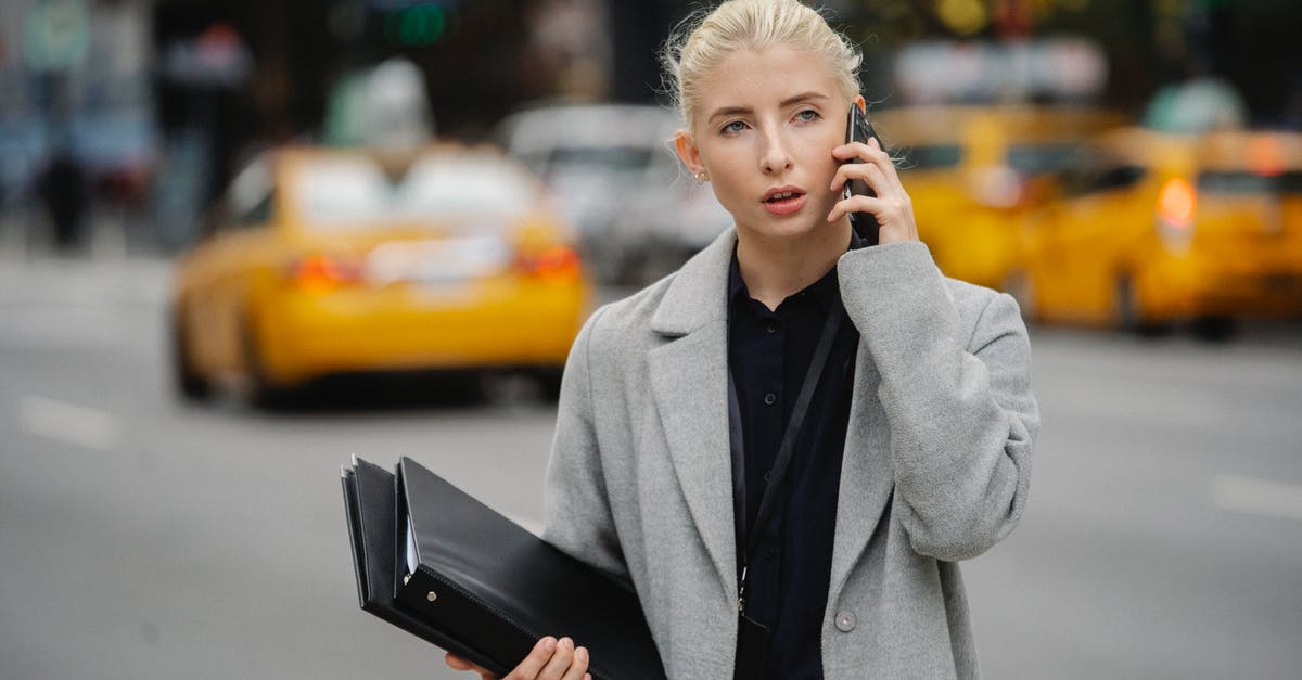 Managing a new, overactive sourdough starter - Focused young businesswoman in gray coat standing on busy street with folders and having conversation on mobile phone