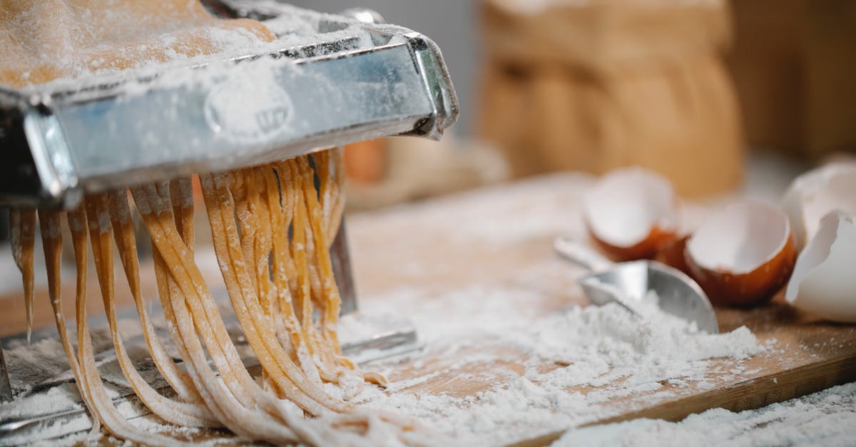Manual noodle press pasta maker sticking - Spaghetti produced from iron pasta cutter on wooden table with eggshell and flour on blurred background
