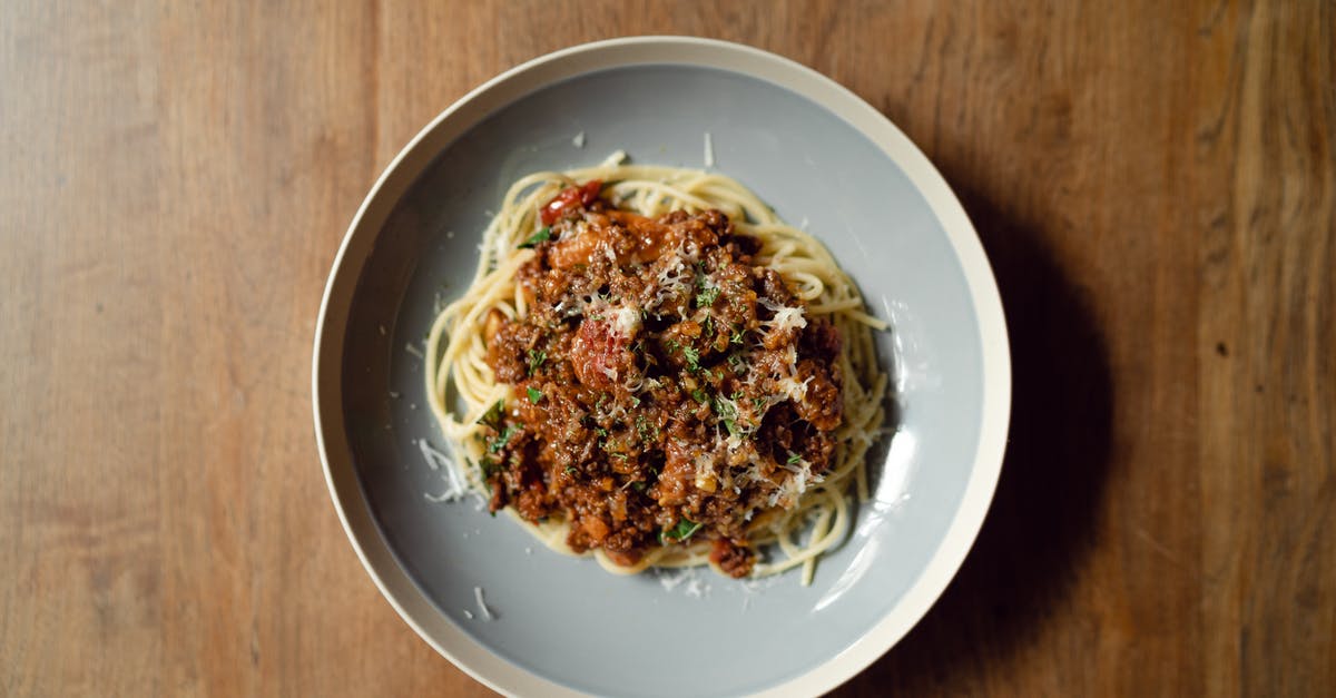 Marinara Sauce recipe - Top view of round plate with delicious Italian pasta Bolognaise garnished with grated parmesan cheese placed on wooden table