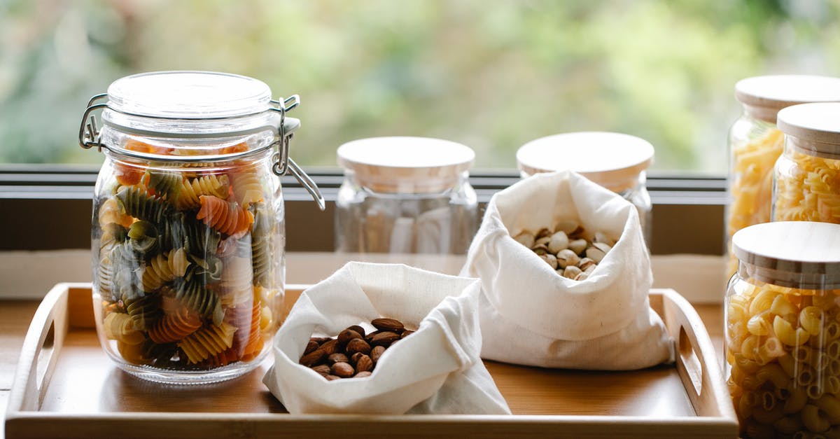 Mascarpone and Almond pasta Sauce? - Glass jar with rotini pasta placed on wooden tray near ECO friendly bags with almonds and pistachios in light room near window on blurred background