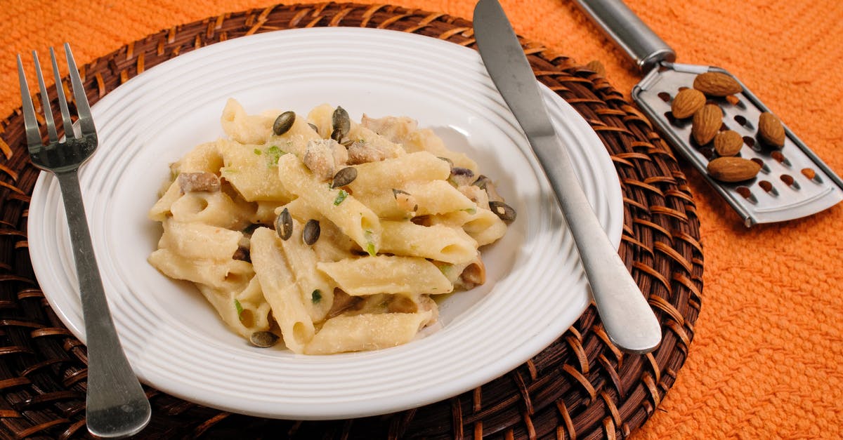 Mascarpone and Almond pasta Sauce? - High angle of tasty homemade pasta under cheese and sunflower seeds in plate with fork and knife near heap of almonds