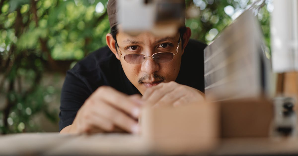 Measure First or Cut First? [duplicate] - Concentrated ethnic craftsman in casual wear in hat and eyeglasses working on workbench with wood plank outside near workshop at daytime