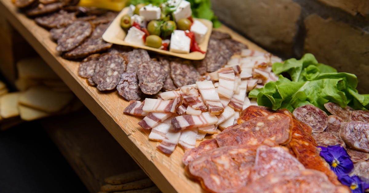 Meat curing vs fermenting - High angle appetizing sliced cured pork fat and smoked sausages served on sideboard with cheese and olives during buffet catering