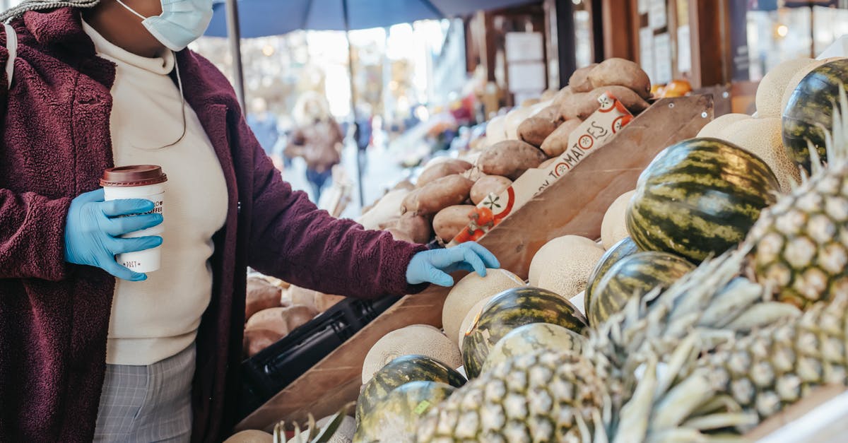 Melon buying tips - Side view of African American female in casual clothes medical mask and latex gloves buying melon in food shop on street