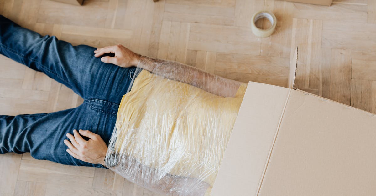 Melted plastic wrap in oven at high temp - From above anonymous male in casual clothing lying on parquet with box on head and upper body wrapped in clingy plastic tape during moving out