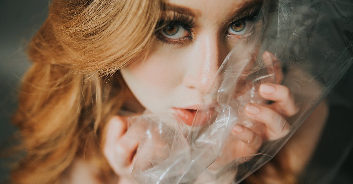 Melted plastic wrap in oven at high temp - From above of young female with blond hair looking at camera with transparent polythene package near face in light room