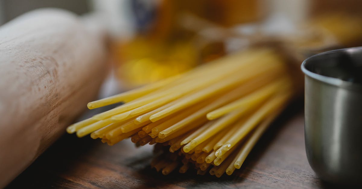 Metal cutlery food pairing - Bunch of uncooked spaghetti near metal bowl and rolling pin placed on wooden surface on light kitchen