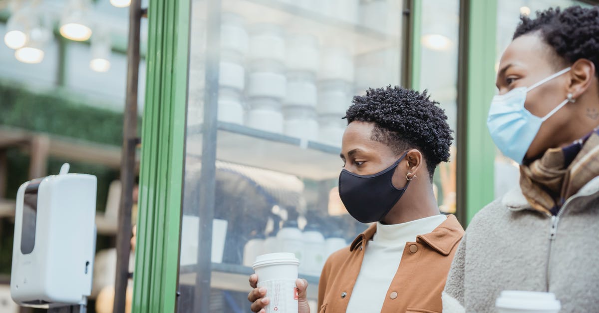 Microwave-safe cups becoming less safe - African American male couple with tasty takeaway hot beverages strolling on street near building while spending time together in city