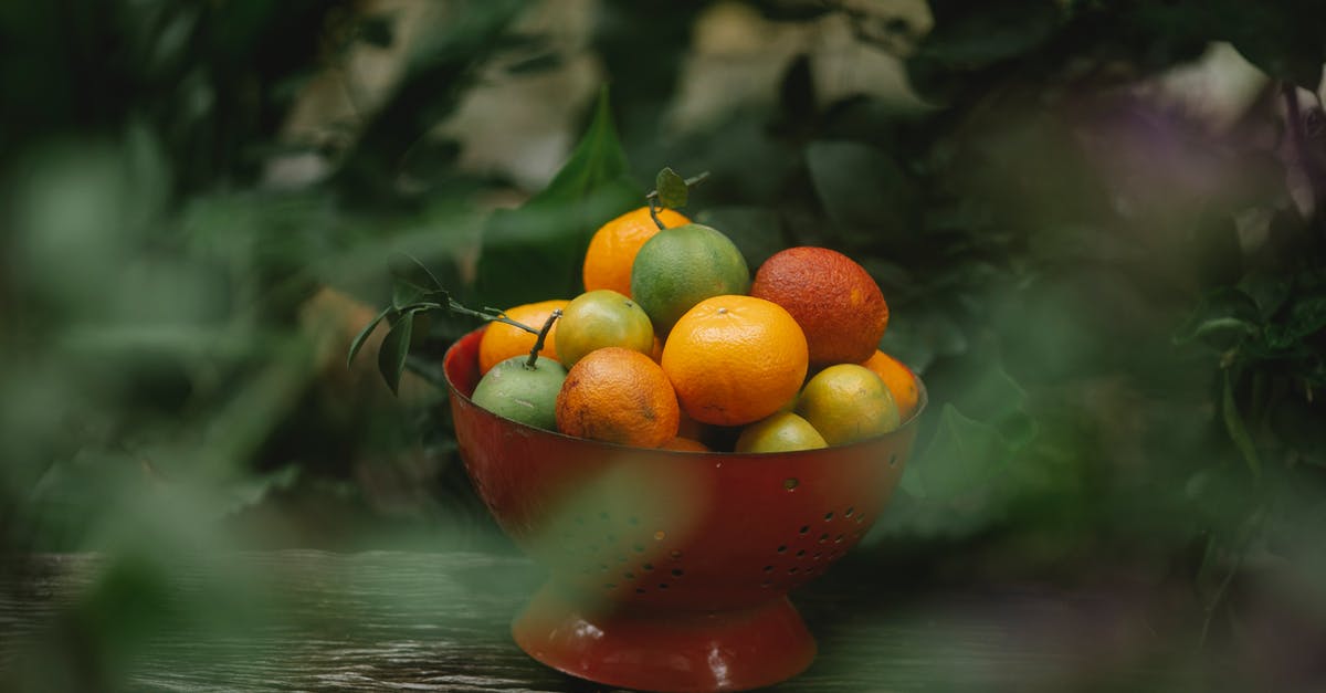 Mimicking Lipton's Green Diet Iced Tea Citrus - View through blurred foliage of fresh ripe oranges and mandarins with other exotic fruits placed in red colander on wooden shelf