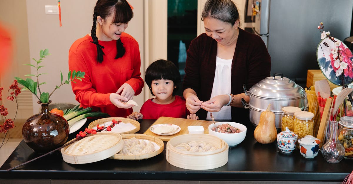 Minced meat malaise - Cheerful Asian grandma with boy and female teen preparing dumplings at table with minced beef filling at home