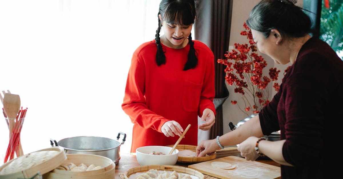 Minced meat malaise - Smiling ethnic grandma with female teen preparing Chinese dumplings while talking at table with traditional steamers in house