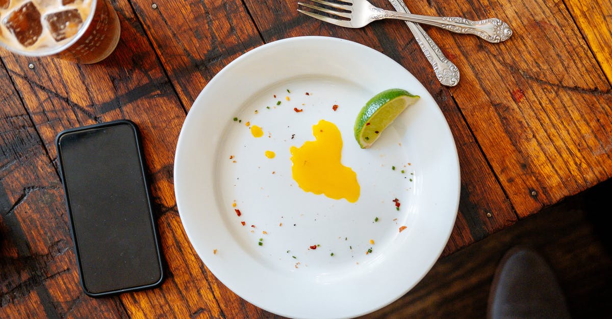 mixed egg and bicarbonate of soda - Top view of white plate with slice of lime an egg yolk placed on wooden table near smartphone and iced drink