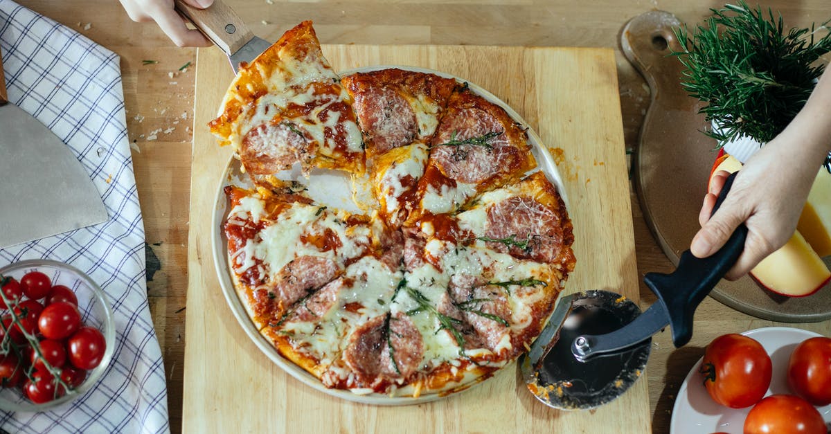 Mold from cheese on sausage, is it safe to eat? - From above unrecognizable women taking slice of pizza with cheese and salami using spatula and cutting with pizza cutter