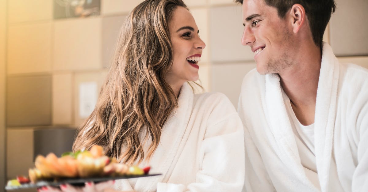 Mug-cake mix at home - Side view of content couple in bathrobes relaxing on bed with platter of mixed fruit and looking at each other