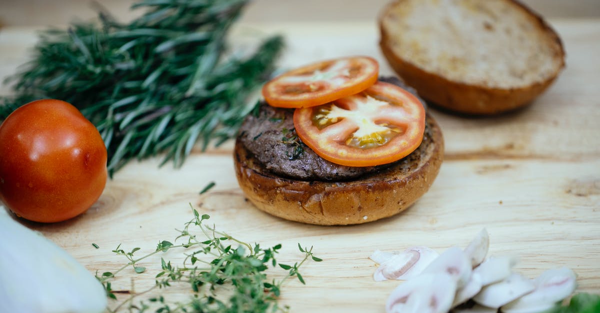 Mushroom replacement in Beef Wellington - Toasted buns with cutlet and tomatoes placed on wooden table with greens and mushroom in kitchen while preparing tasty burger